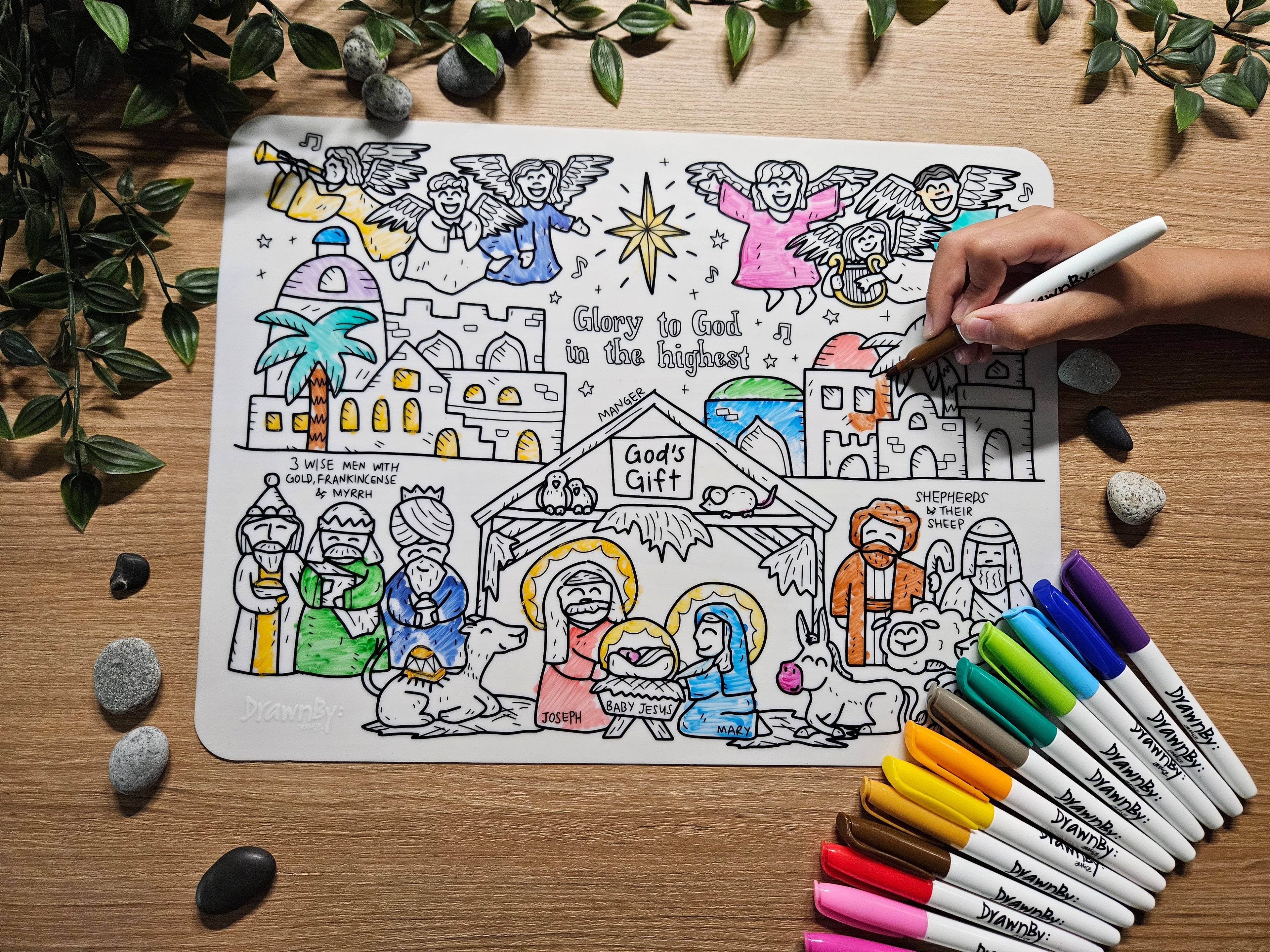 DrawnBy: God's Gift Bible Story Coloring Mat of a Nativity scene with markers on a wooden surface