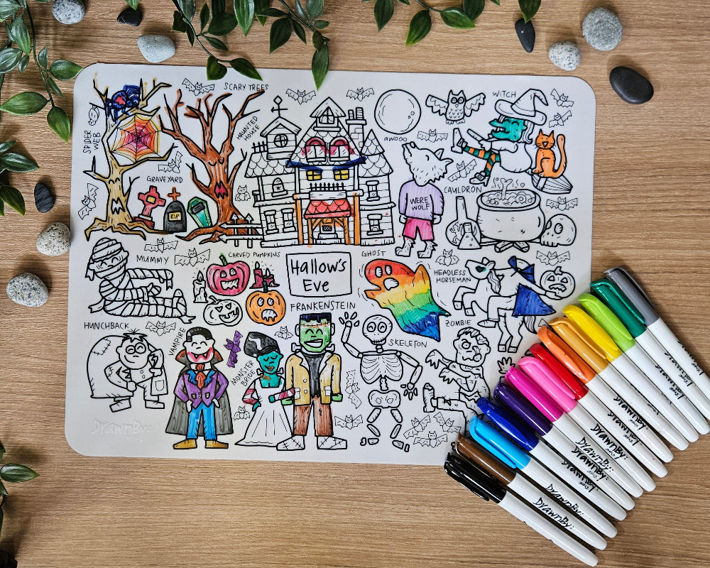 DrawnBy: Hallow's Eve Colouring Mat with markers on a wooden table next to a plant