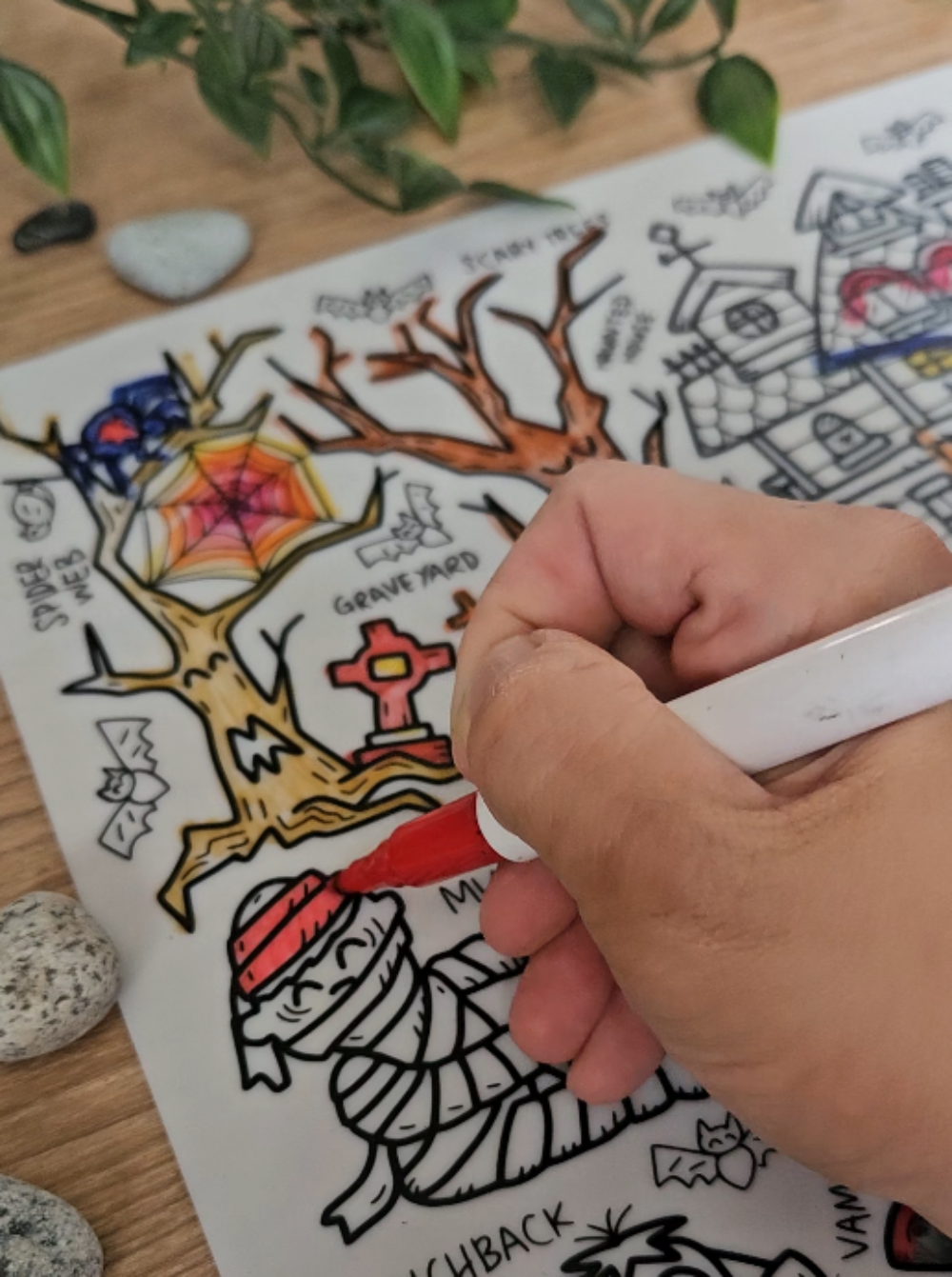 DrawnBy: Hallow's Eve Colouring Mat with Halloween-themed illustrations and a hand coloring one of them.