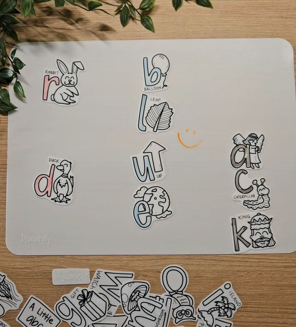 Children's alphabet stickers on a white mat with scattered stickers on a wooden surface.